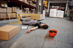 Man who has fallen in warehouse near a caution sign for wet floors