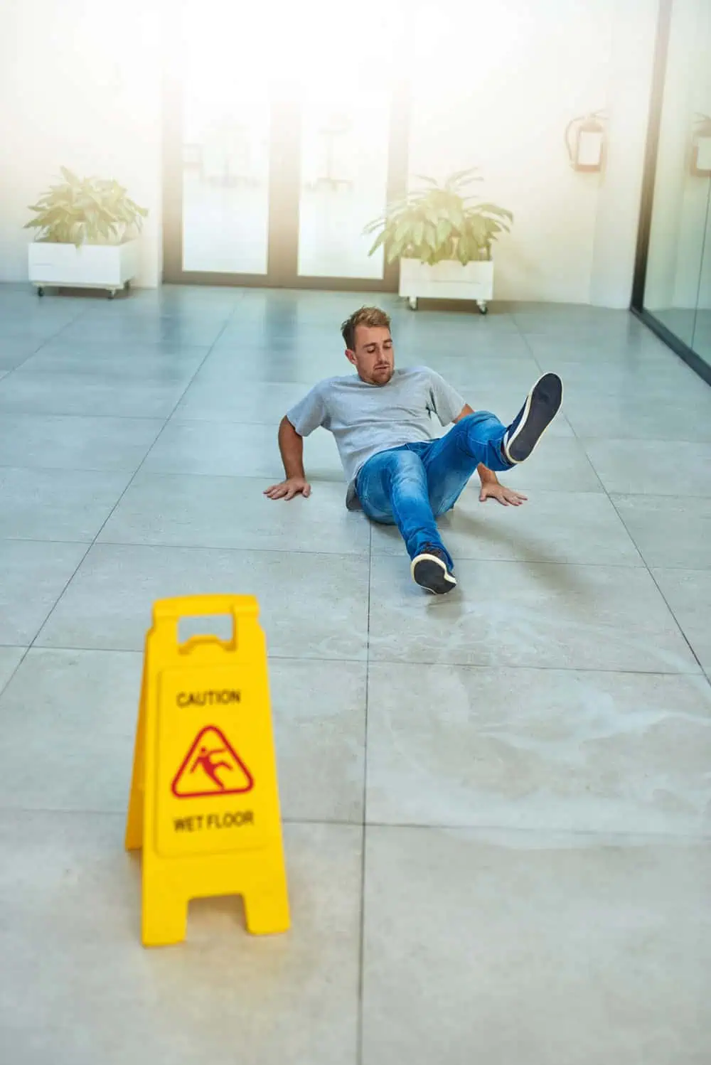 Premises Liability for Property Owners casually dressed man on floor after a fall near a caution sign.