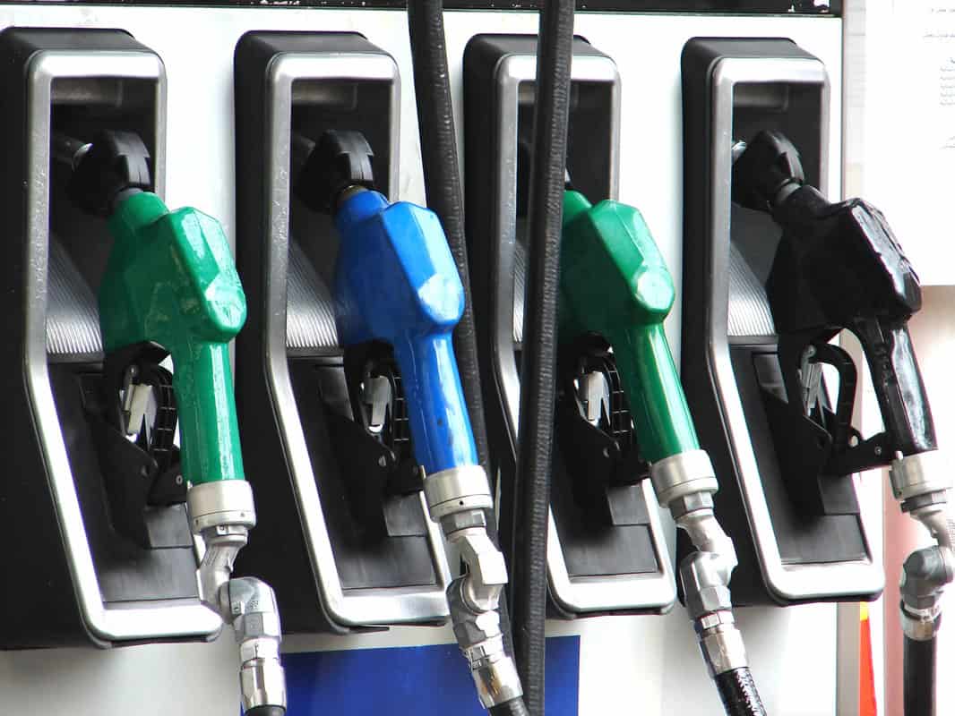 Four fuel pump nozzles—two green, one blue, and one black—are shown at a gas station pump, each in its holder.
