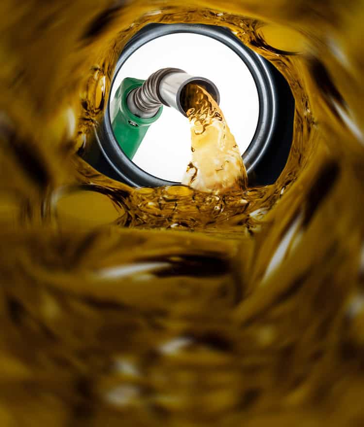 Close-up view from inside a tank showing fuel being poured from a green nozzle, with liquid splashing around the nozzle opening.
