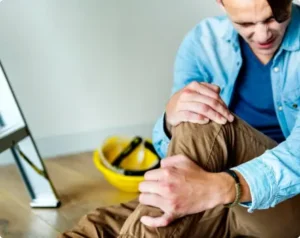 man holding knee in pain. hard hat and ladder on floor in background