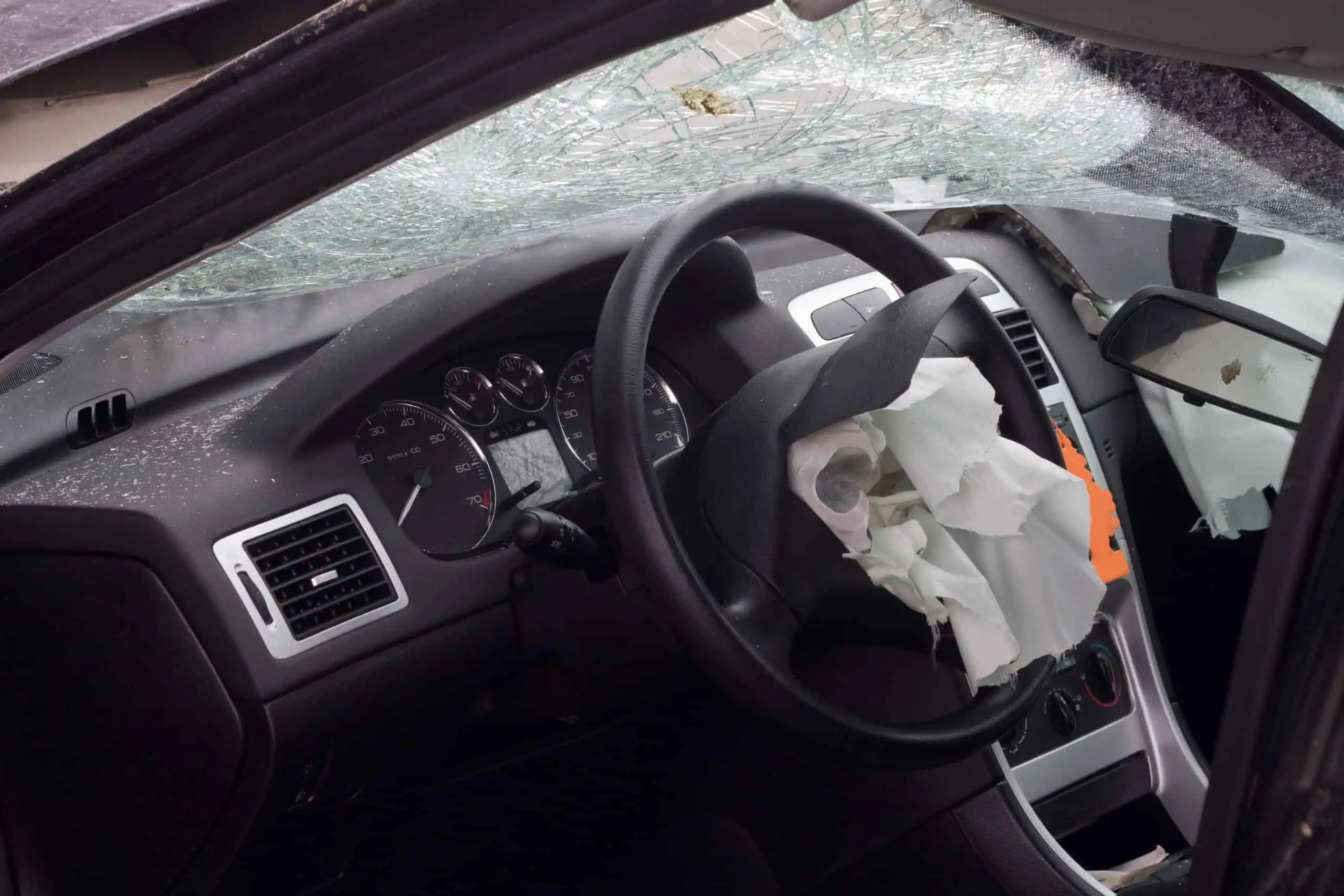 Interior of a car with a shattered windshield and deployed airbag, indicating recent collision or accident.