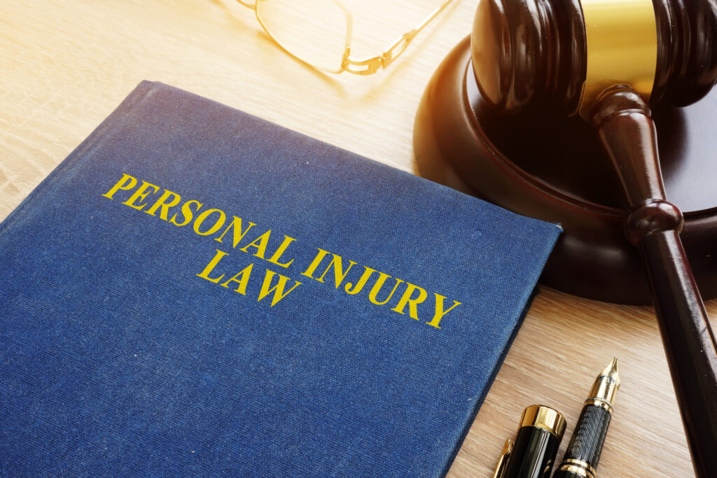 A book titled "Personal Injury Law" sits on a desk next to a gavel, eyeglasses, a fountain pen, and a notepad.