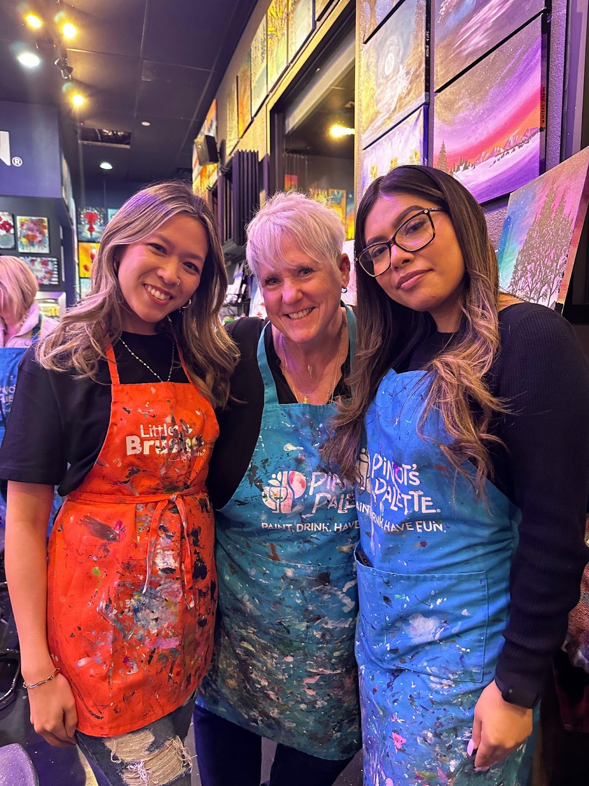 three women posed together with painting smocks on