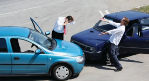 Two cars have collided at an intersection. Two men in business attire stand near the cars, appearing to argue and gesture about the accident.