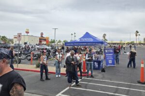 People stand near a blue Shook & Stone tent in a parking lot with motorcycles parked and a McDonald's visible in the background.