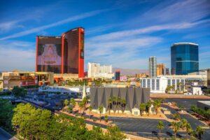 View of modern buildings and hotels on the Las Vegas Strip under a clear blue sky, with palm trees and a church in the foreground.