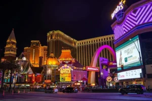 Las Vegas Strip at night showing brightly lit hotels, casinos, restaurants, and colorful neon signs, including Venetian, Harrah's, and Casino Royale.