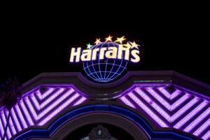 Illuminated Harrah's casino sign with colorful stars and a globe above a purple-lit building facade at night.