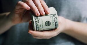 A person holds and counts a thick stack of U.S. fifty dollar bills with both hands.
