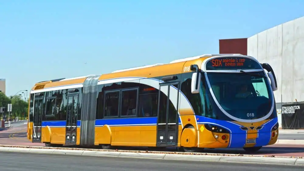 A gold and blue articulated city bus labeled "SDX Downtown & Strip Express" is stopped at a bus station on a clear day.