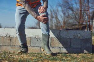 construction worker clutching injured knee at outdoor job site