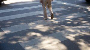 Person walking across a crosswalk with dappled sunlight and shadows.
